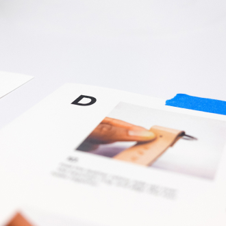 An open book in perspective on a white background. The page shows the letter 'D' and a photo of a leather belt